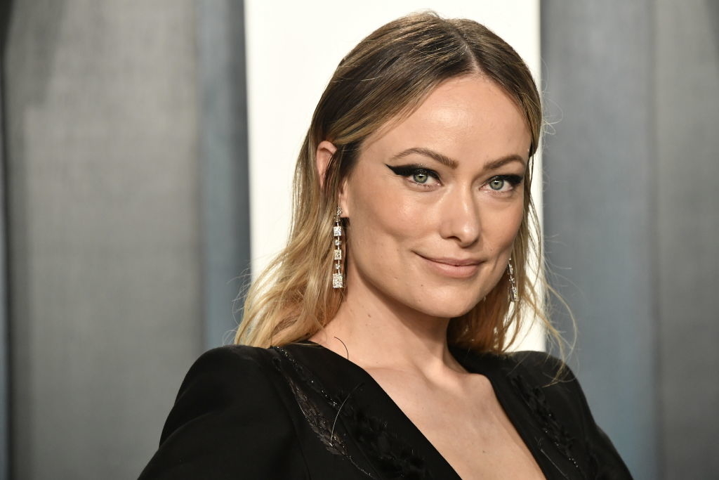 Close-up of Olivia Wilde in a black outfit with long earrings, smiling at an event