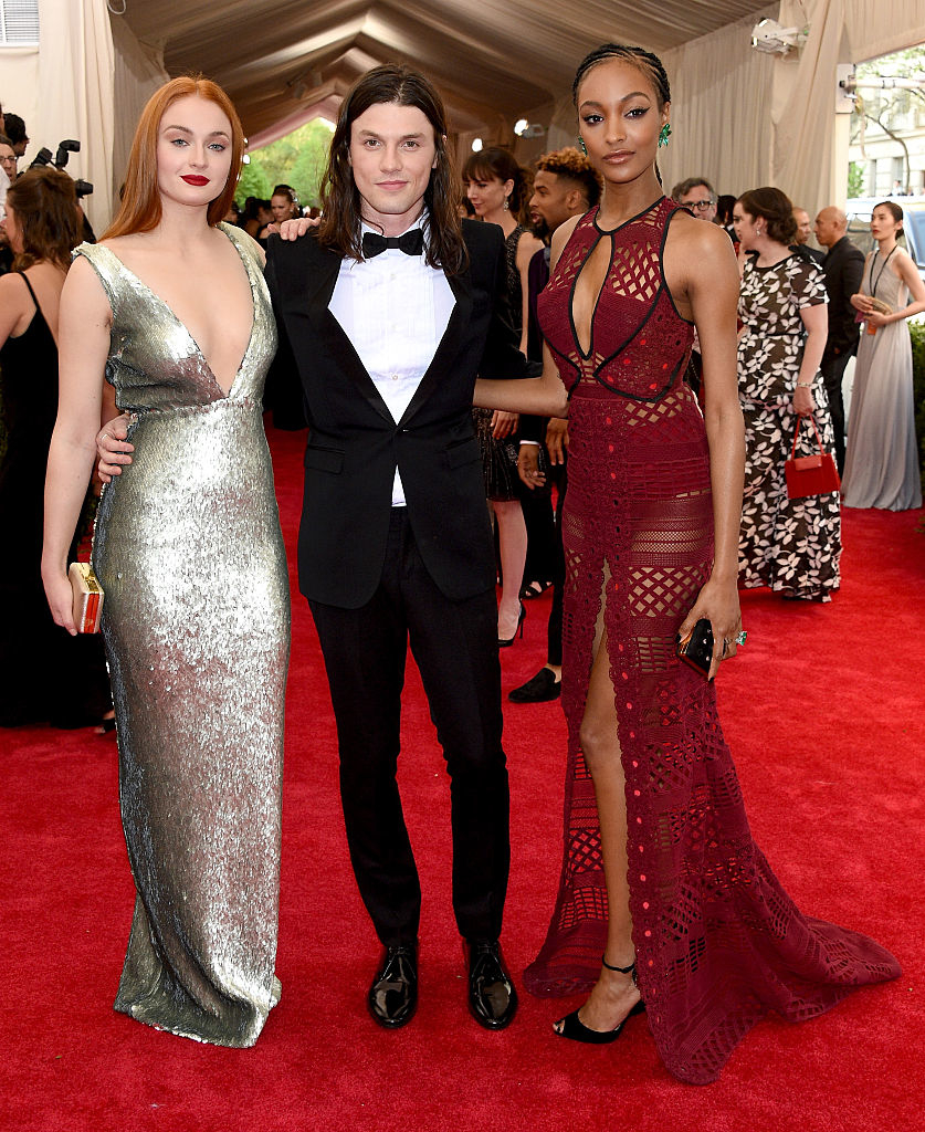 Three celebrities on red carpet; two in shimmering gowns, one in classic tuxedo