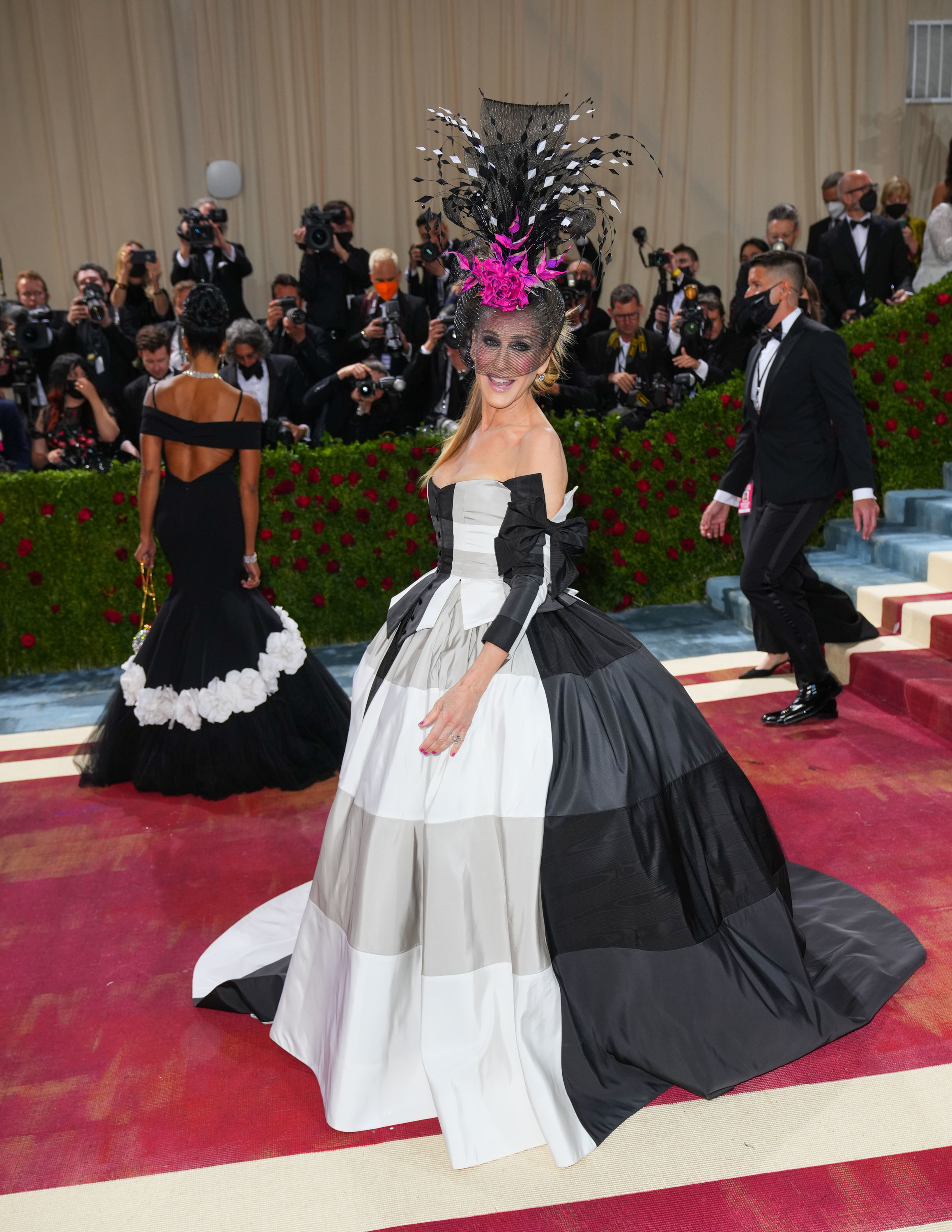 Person in elaborate black and white gown with voluminous skirt and striking feathered headpiece poses on steps at an event