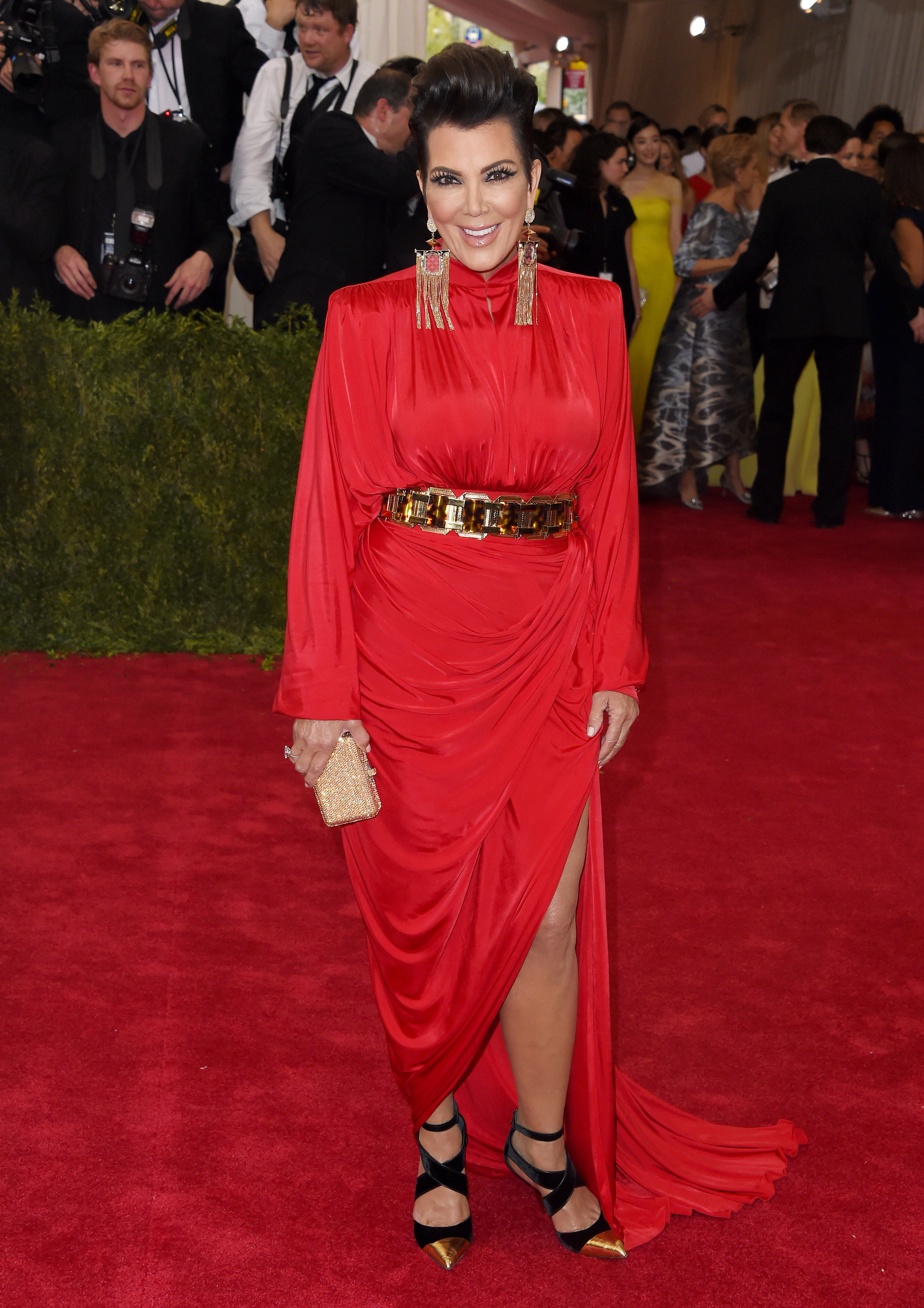 Kris Jenner in a red dress with a thigh-high slit, gold belt, and large earrings at an event