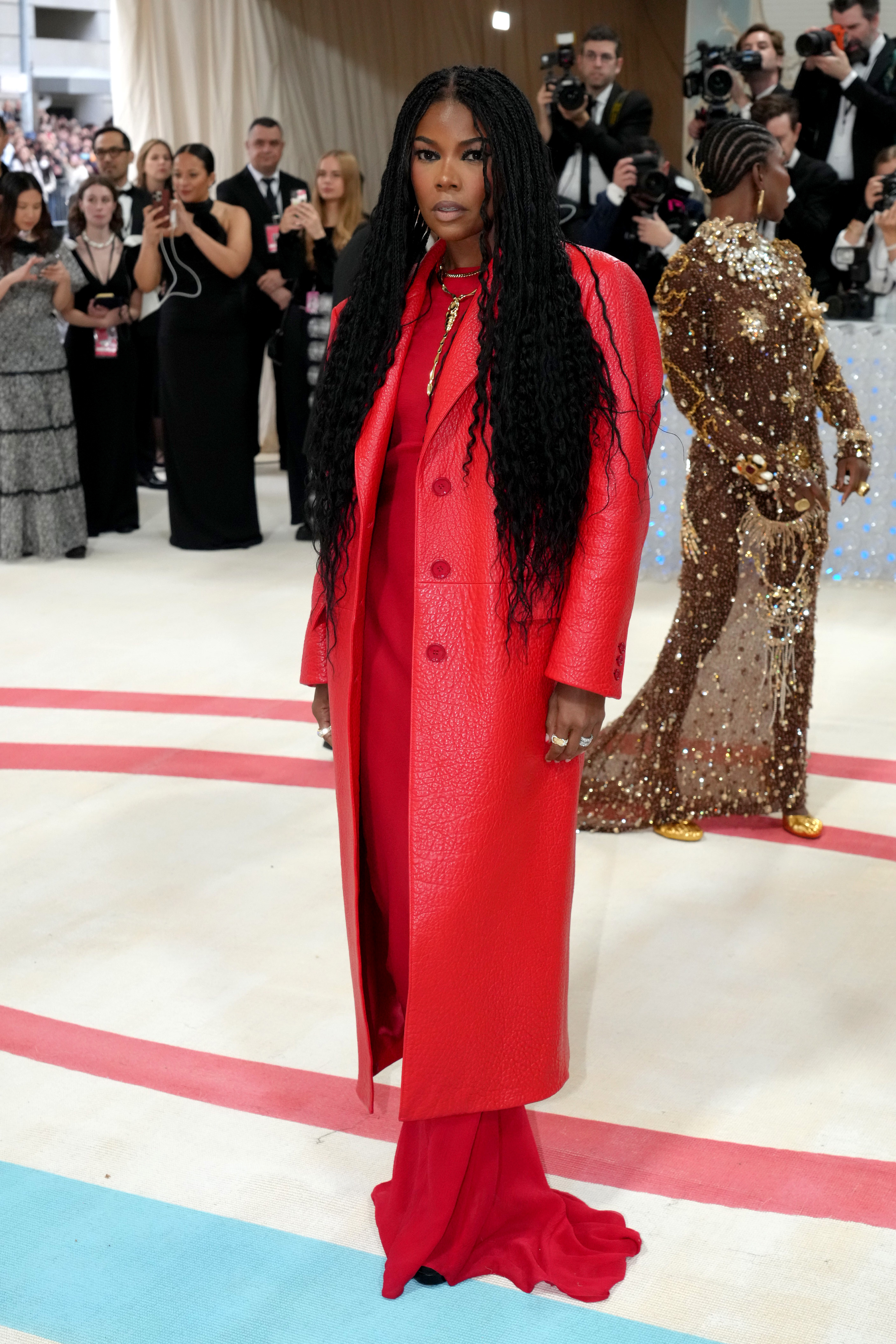 Celebrity in a red coat and dress on the red carpet with onlookers in background