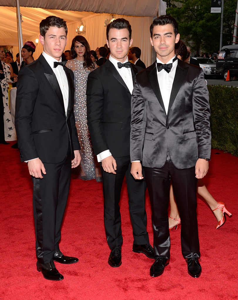 Three men in formal black suits and bow ties stand together