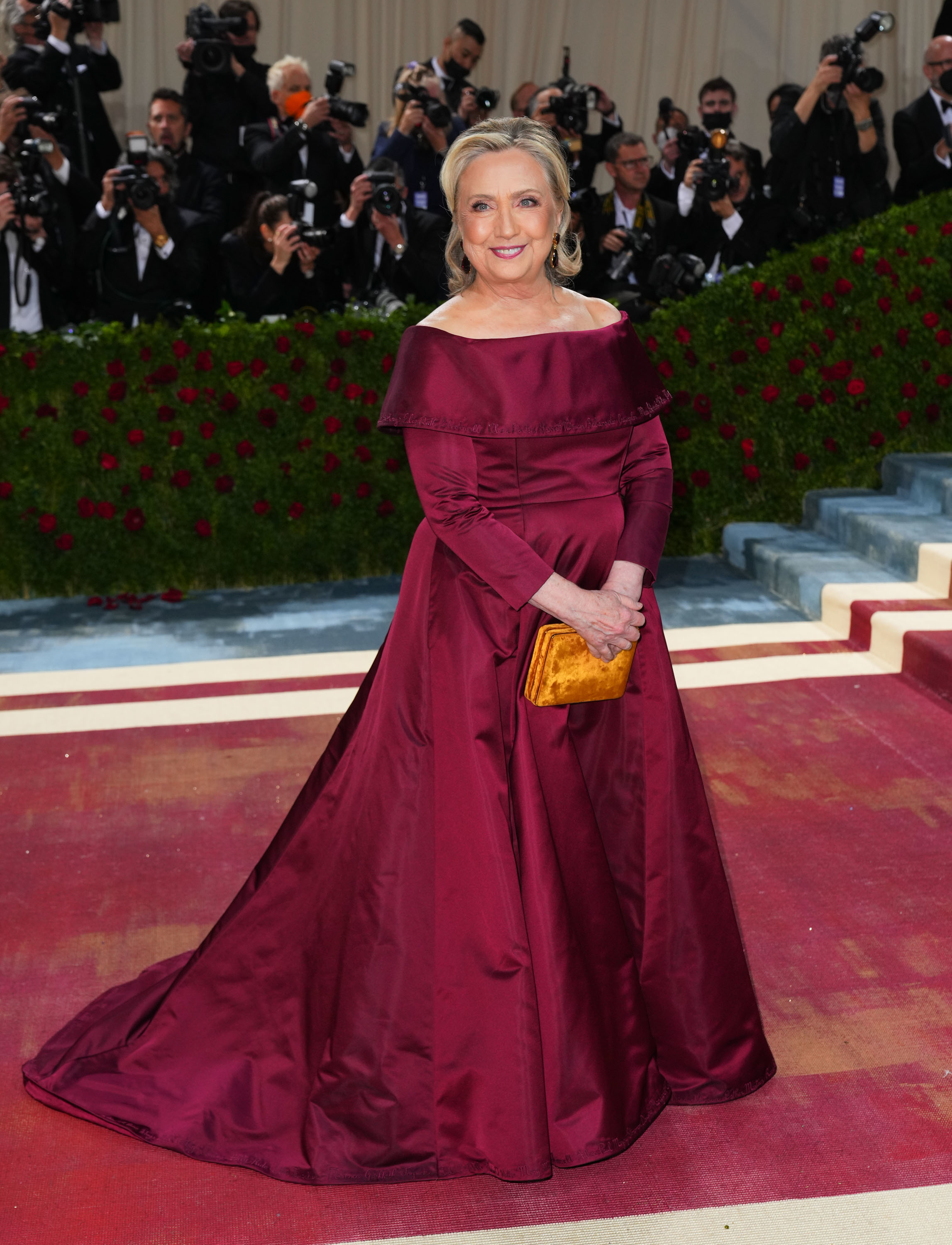 Celebrity in an off-shoulder burgundy gown with photographers in the background