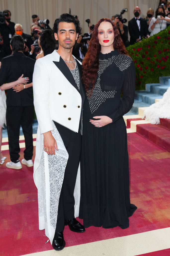Two celebrities at an event, one in a black and white suit, the other in a long-sleeved black gown