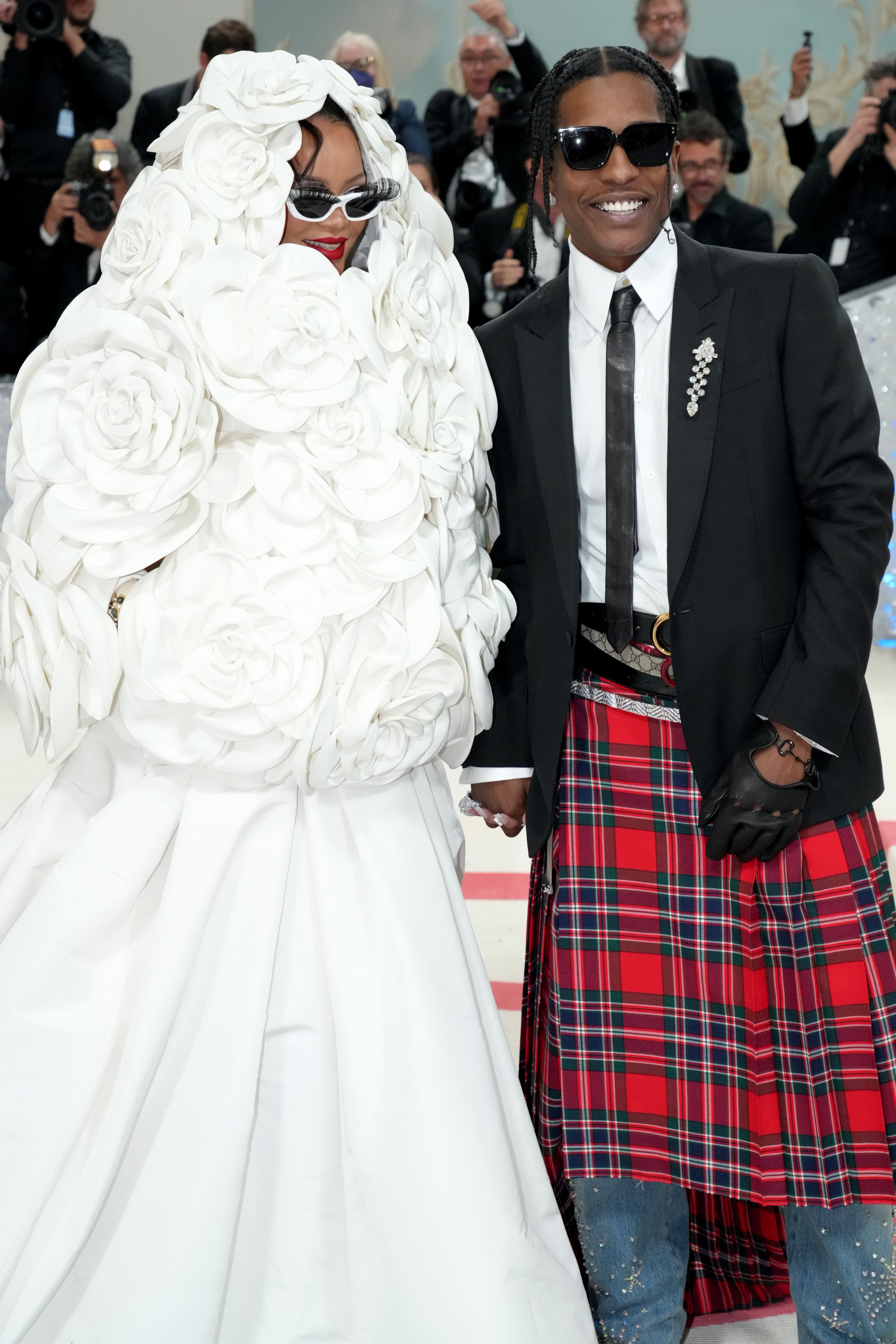 Person in voluminous white floral outfit beside person in tartan kilt and black jacket at event
