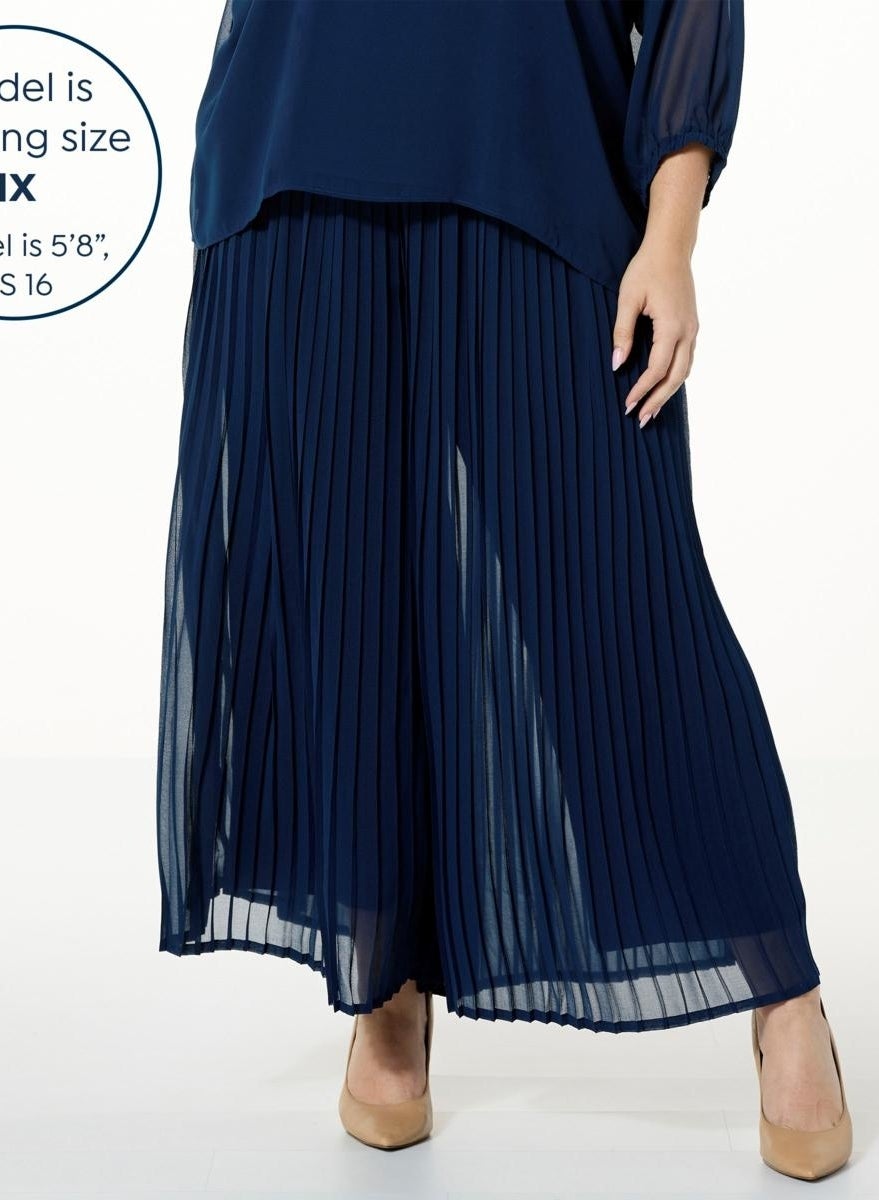 A model wearing a navy pleated pants with skirt overlay and matching blouse