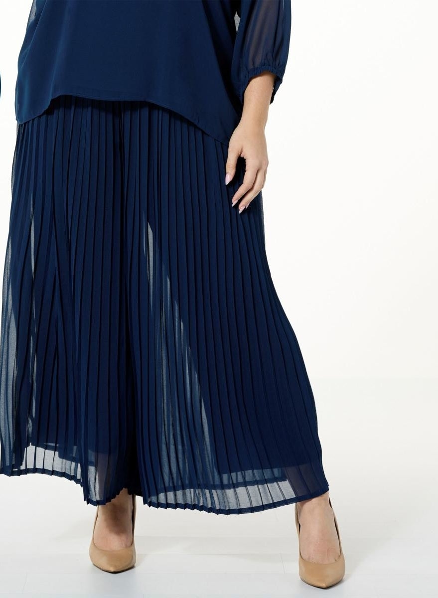 A model wearing a navy pleated pants with skirt overlay and matching blouse