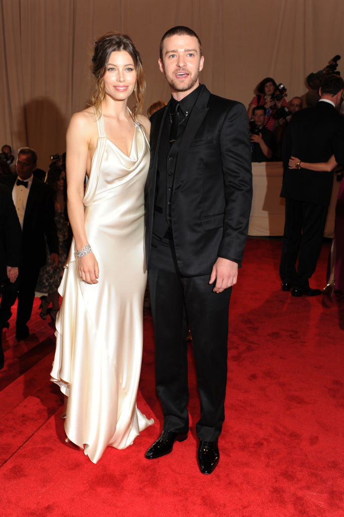 Two people posing on a red carpet; one in a satin gown and the other in a black suit with a bow tie