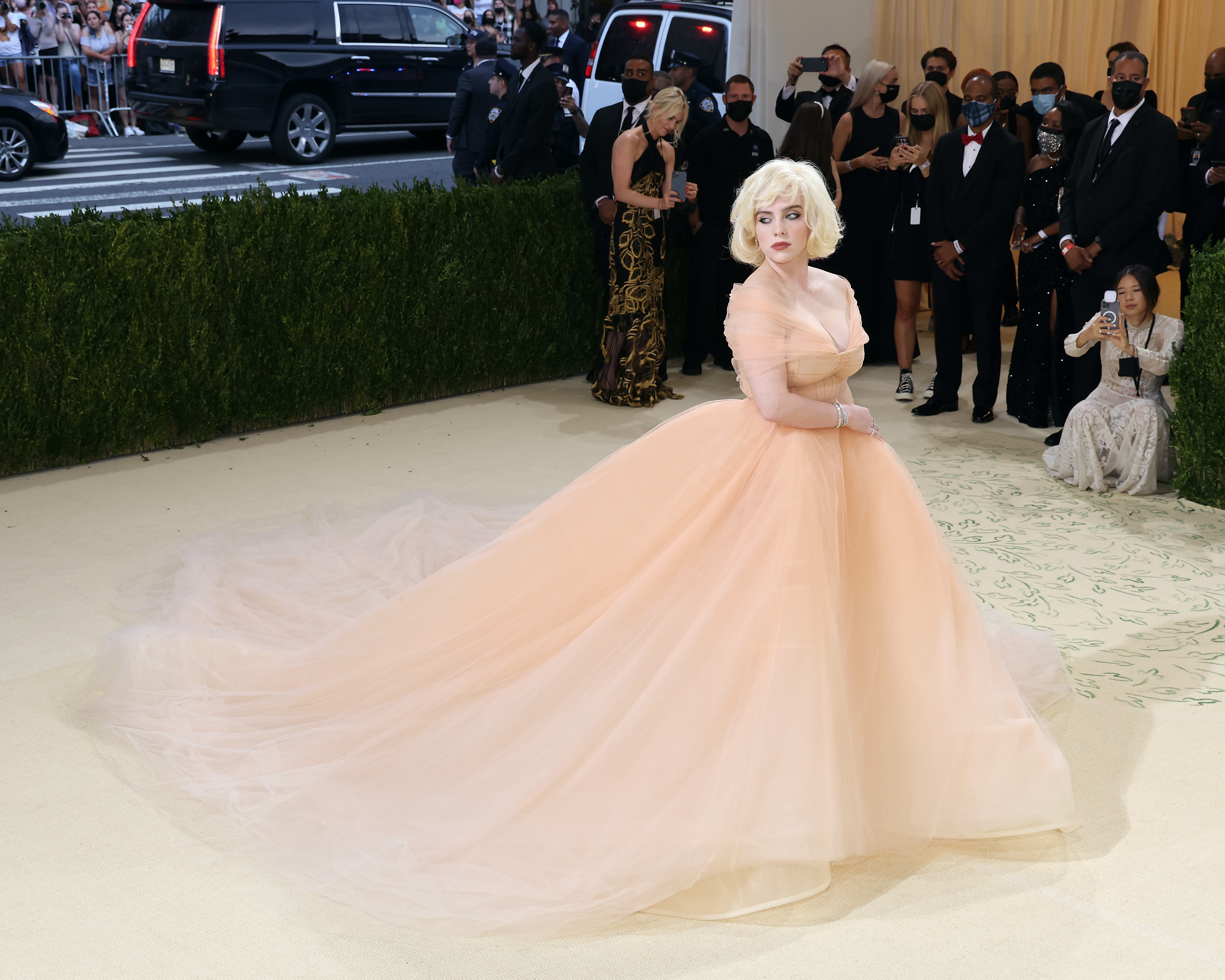 Person in voluminous peach gown and short blonde wig on red carpet