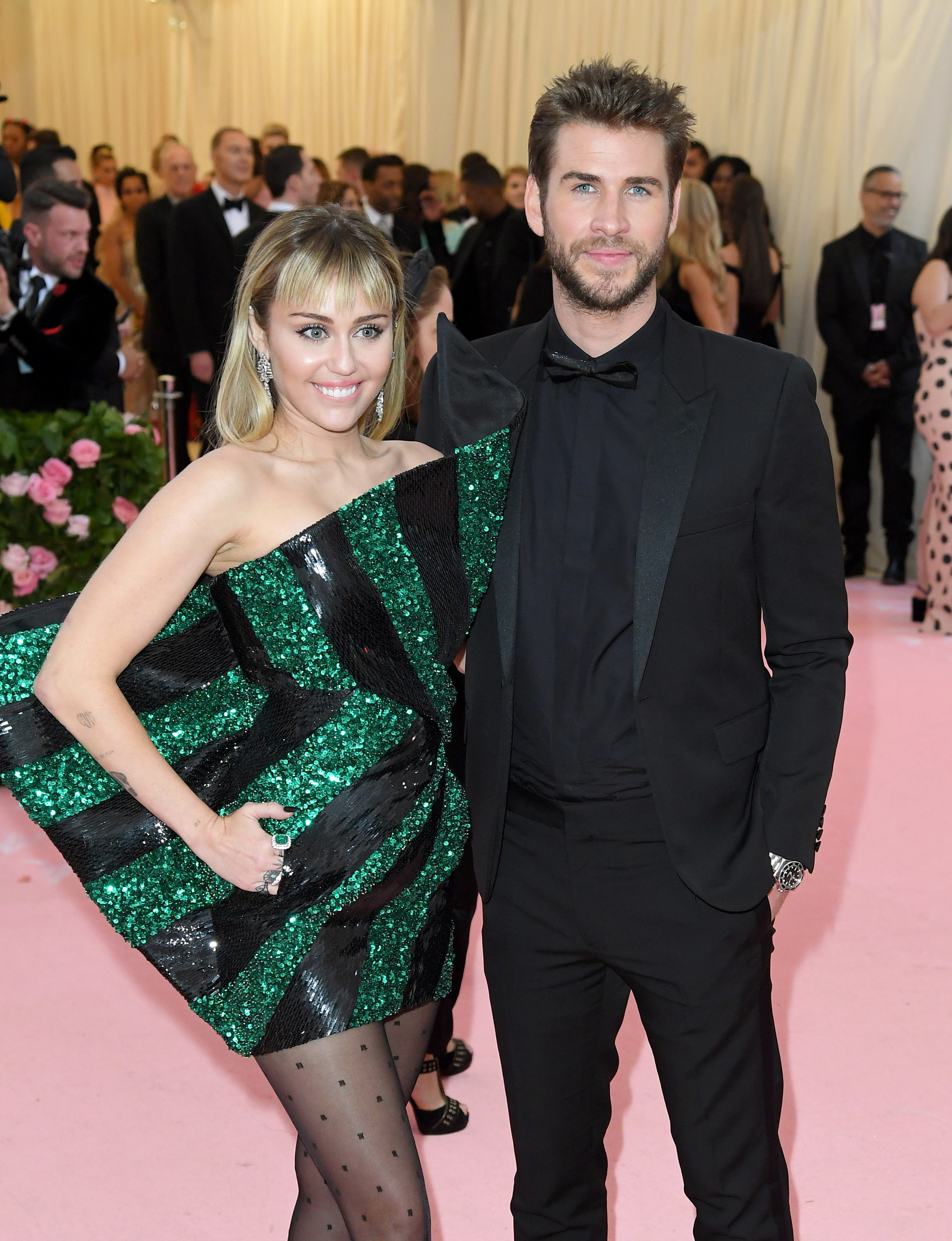 Miley Cyrus in a green and black sequined dress with Liam Hemsworth in a black suit on a gala event