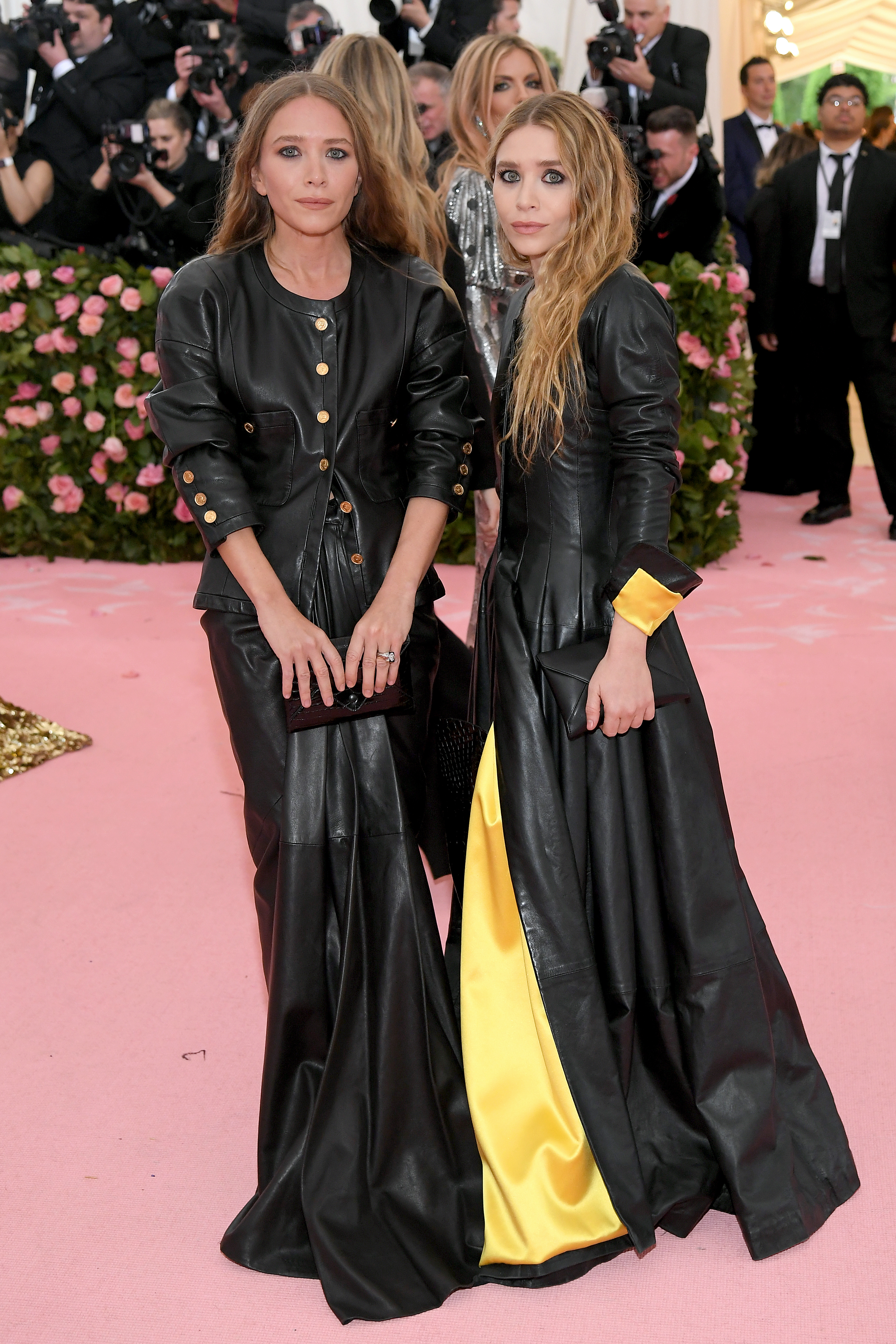 Two individuals standing together in matching leather outfits with a yellow accent on one sleeve at a formal event