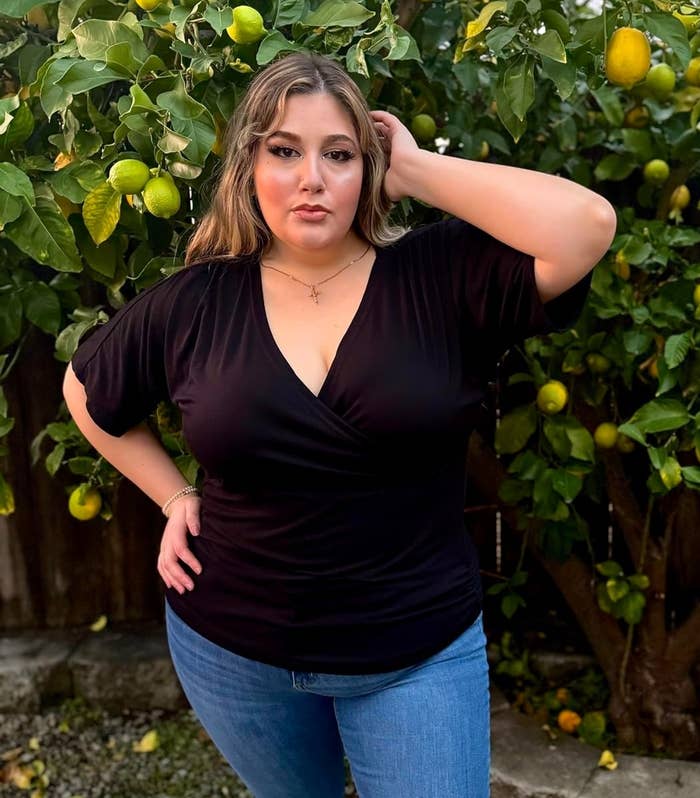 reviewer posing with hand in hair in front of a lemon tree, wearing a black v-neck top and jeans