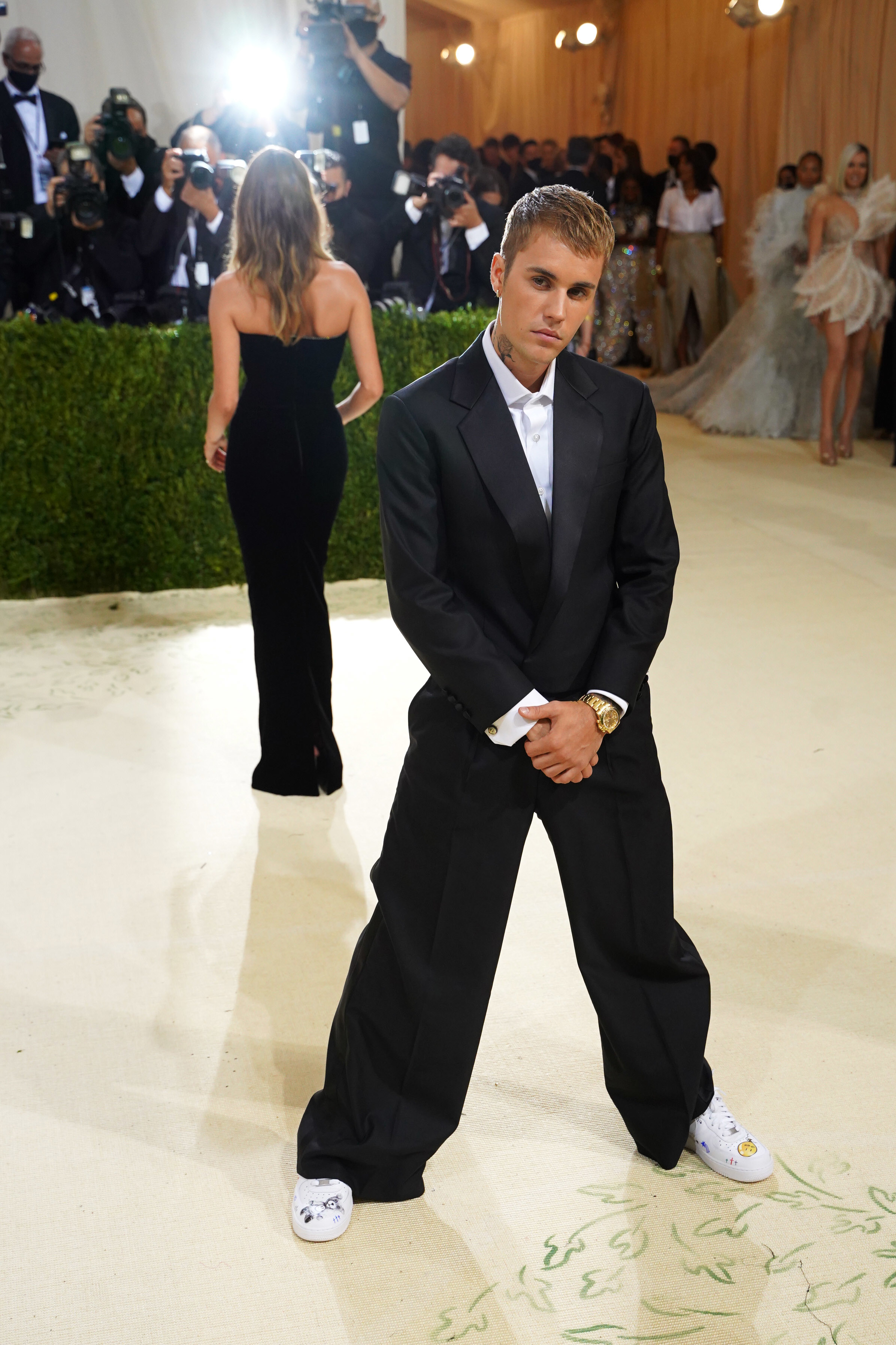 Justin Bieber in a classic black suit with bow tie, standing on a carpet, cameras in the background
