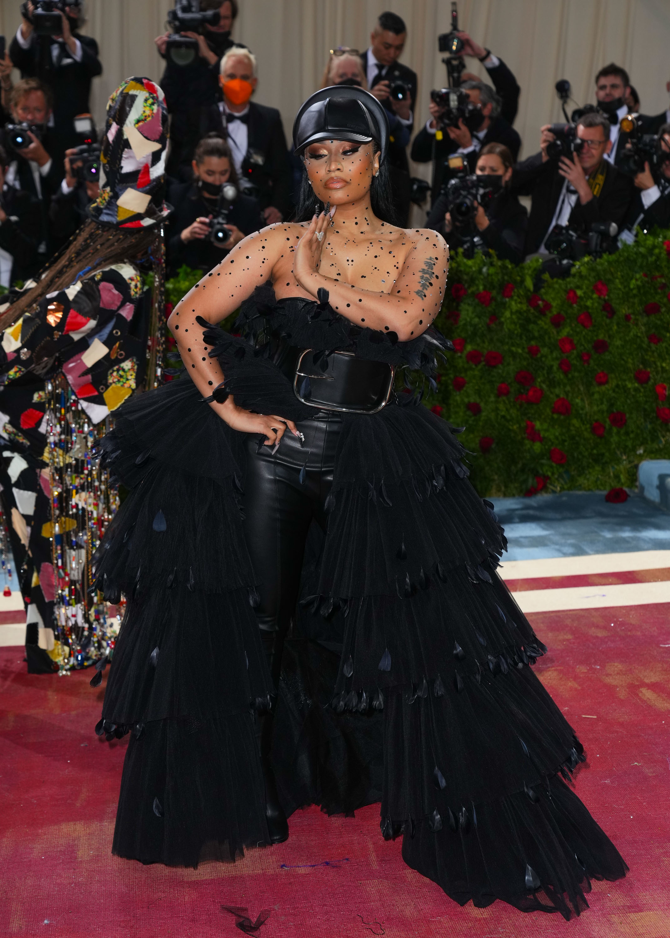 Nicki Minaj at an event wearing a black, ruffled outfit with belt and embellishments, posed on the red carpet