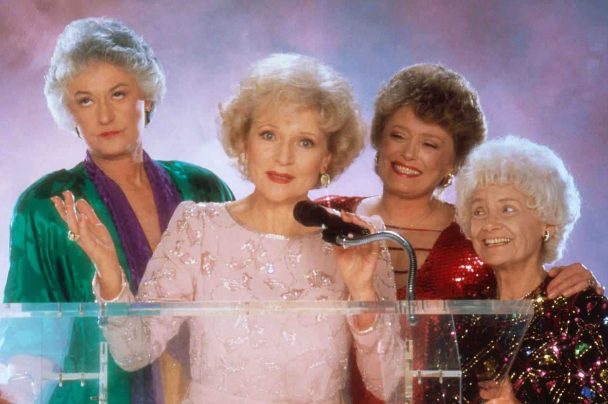 Four characters from 'The Golden Girls' standing together, one holding a microphone, in formal attire
