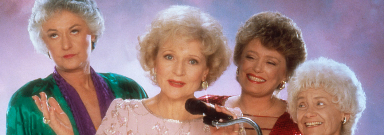 Four characters from 'The Golden Girls' standing together, one holding a microphone, in formal attire
