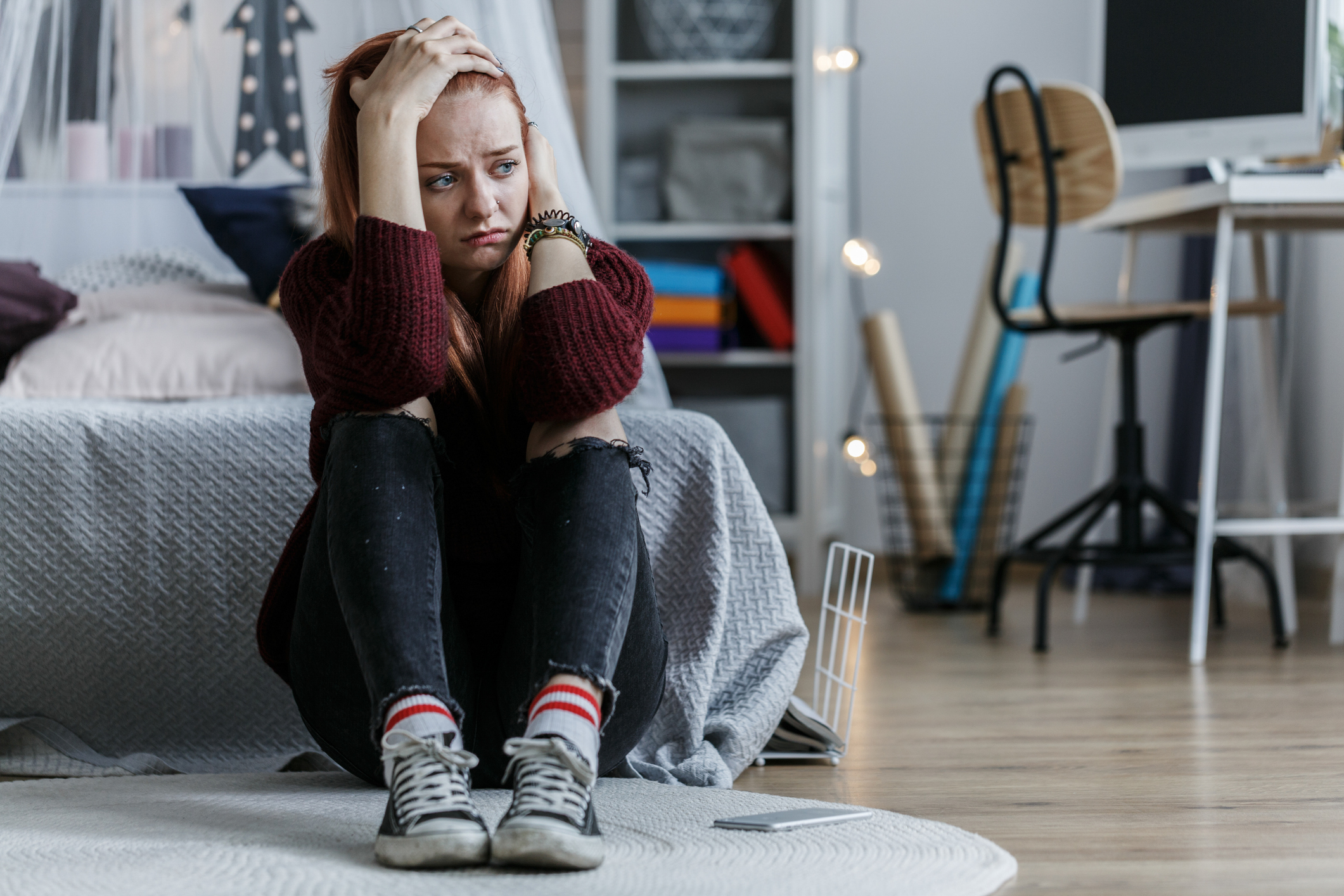 Adult in a sweater and jeans sits on the floor looking worried, with a child&#x27;s room in the background