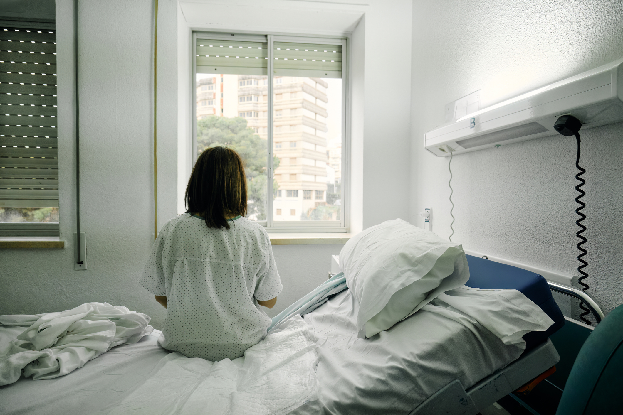 Person sitting on a hospital bed looking out the window, suggesting themes of health and parenting