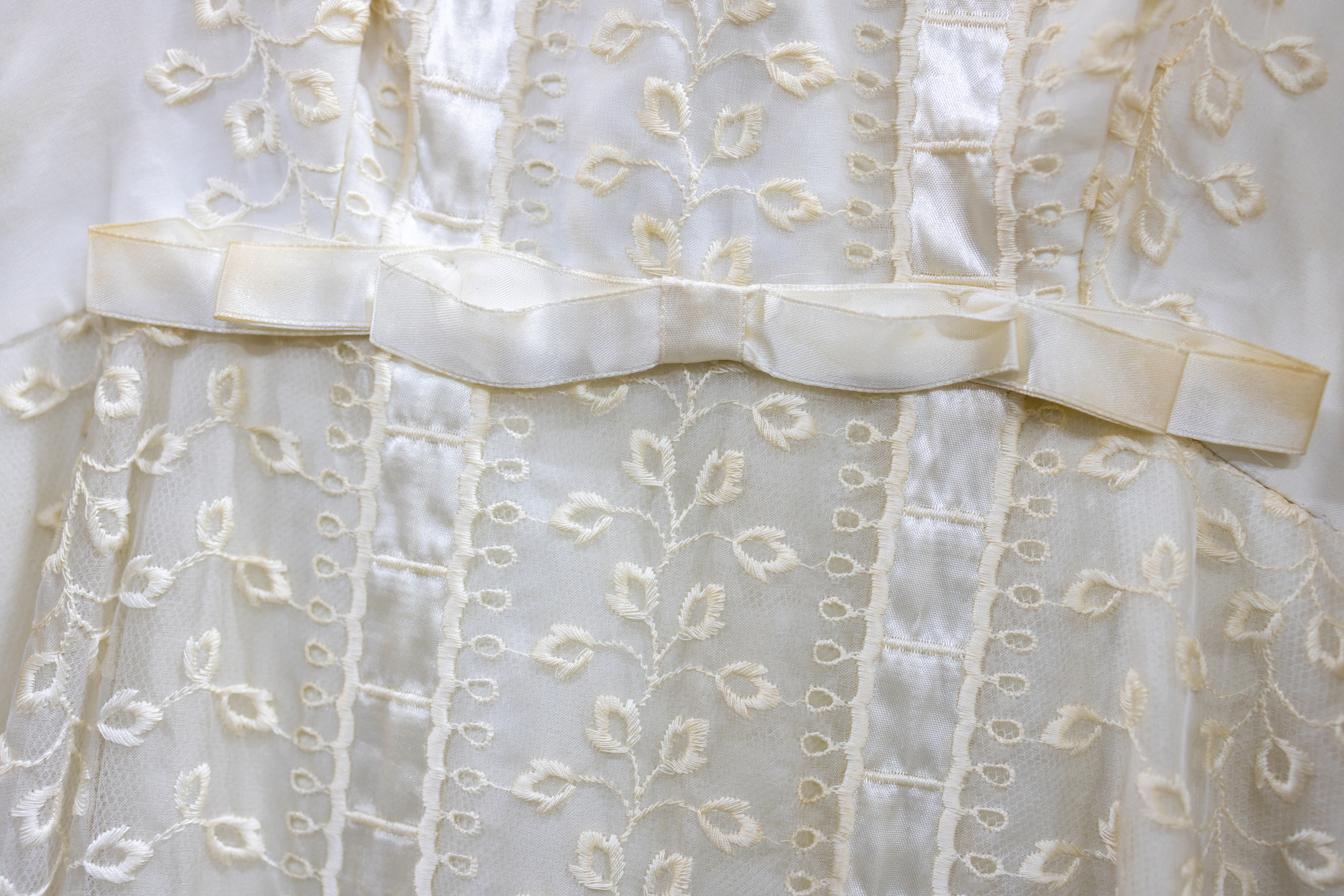 Close-up of a child&#x27;s white dress with embroidered floral pattern and satin ribbon