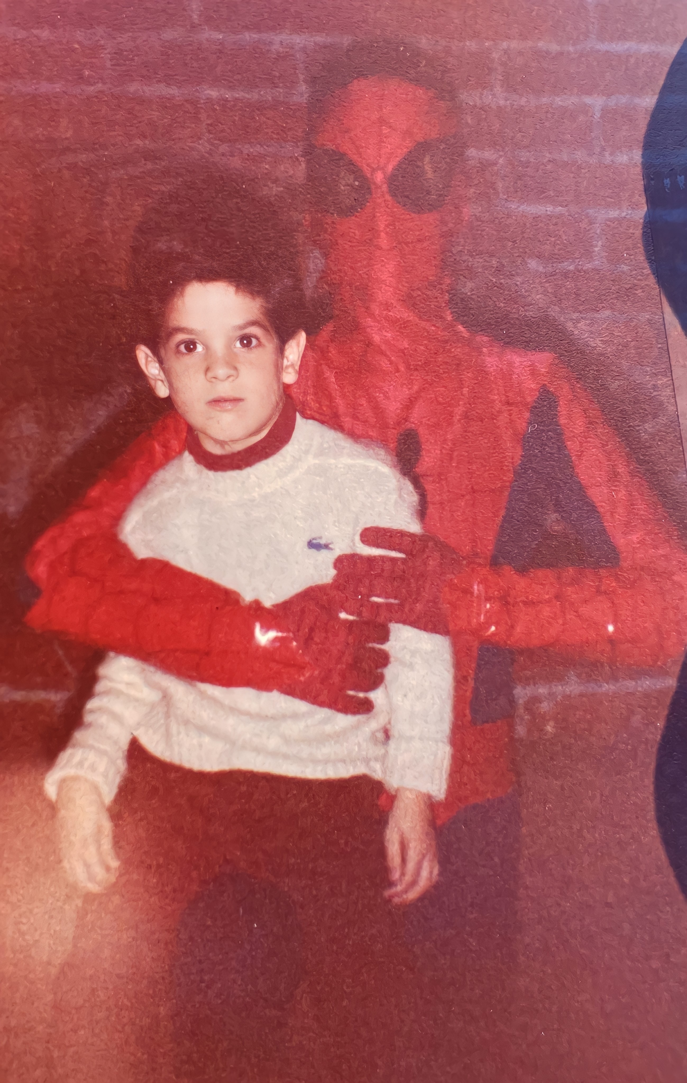 Child in a white sweater with a person dressed as Spider-Man. Vintage photo aesthetic, evoking nostalgia