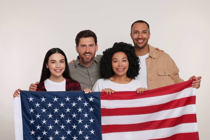 Four smiling friends holding a US flag together, expressing unity and patriotism