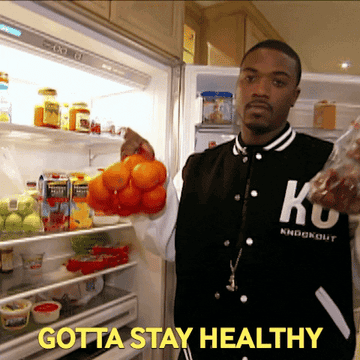 Man in varsity jacket holding oranges near an open fridge, conveying a healthy lifestyle message