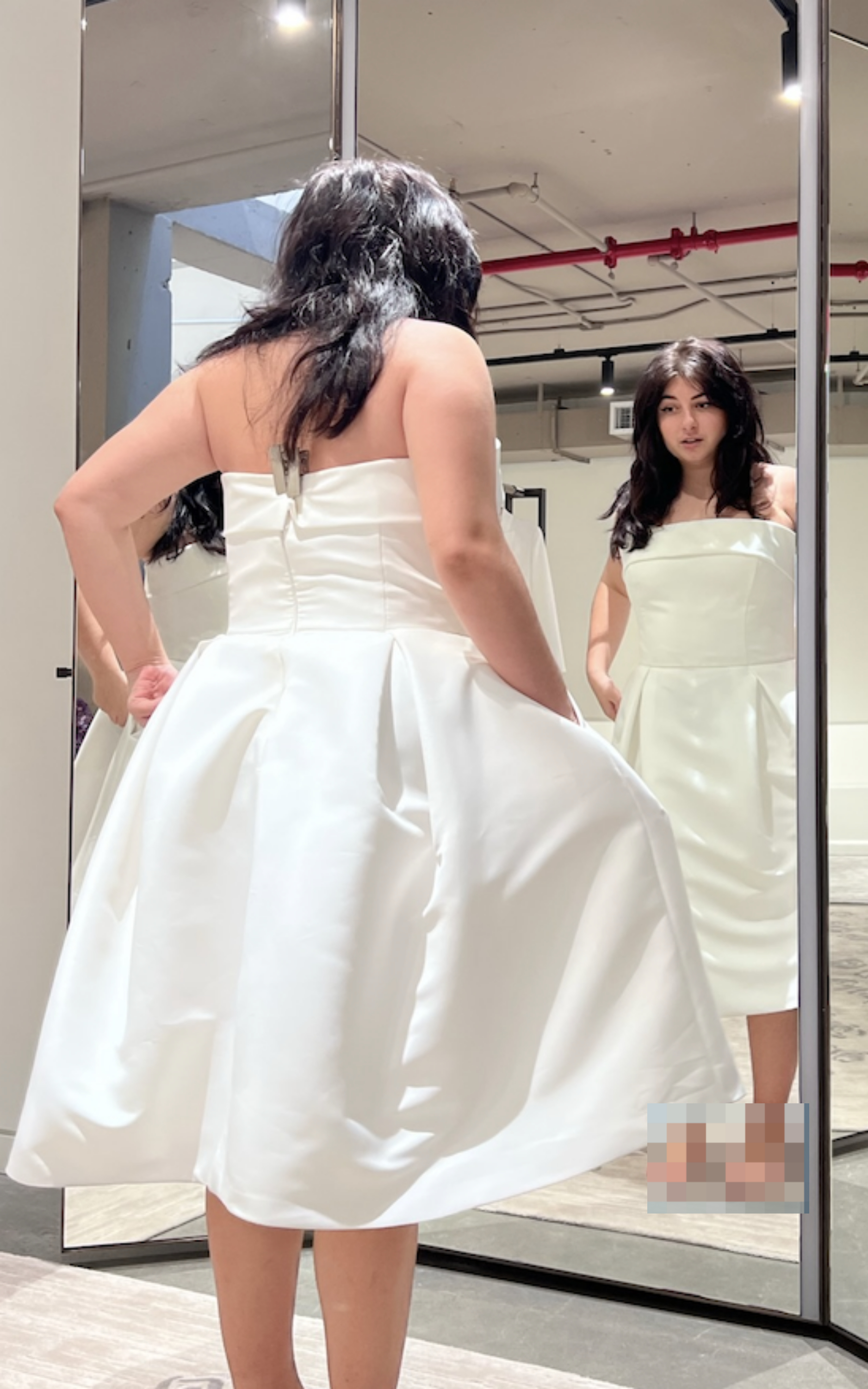 Woman in white dress examines her reflection in a full-length mirror