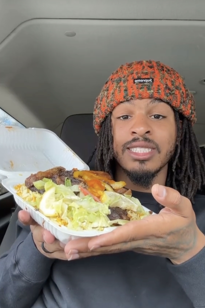 Keith Lee holding a take-out container with a mixed salad and meat, wearing a beanie, smiling at camera