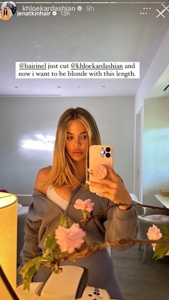 Khloe Kardashian takes a mirror selfie wearing a gray outfit, fresh haircut, with cherry blossoms in the foreground