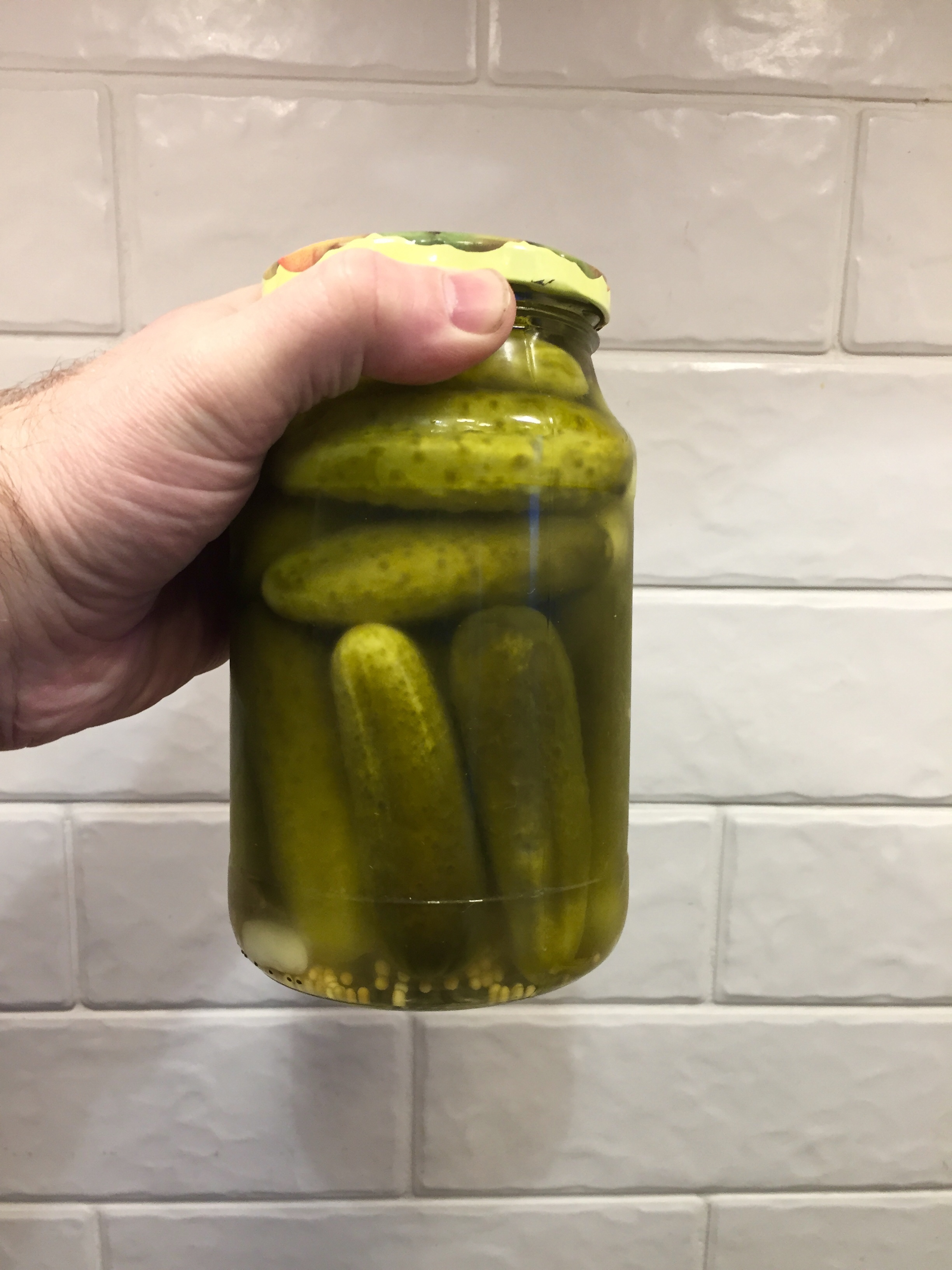 Hand holding a jar of pickles against a tiled background