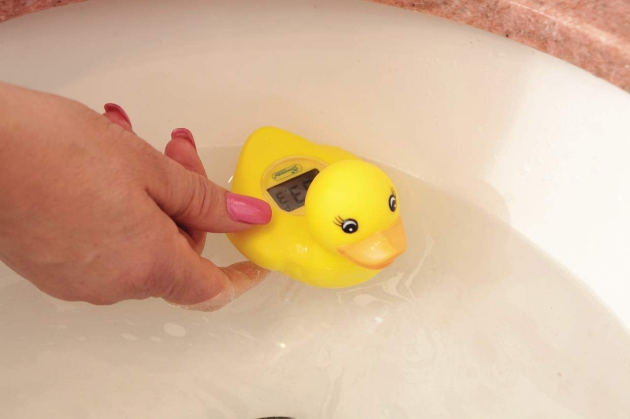A hand holding a yellow rubber duck with a built-in thermometer in water; suitable for bath time temperature checking