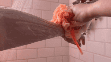 Person lathering arm with a bath loofah in the shower