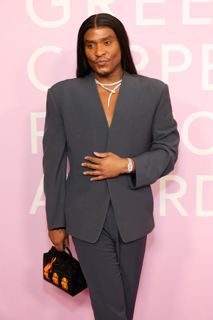 Law posing on red carpet wearing a blazer, hand on stomach, with a jeweled necklace and a handbag