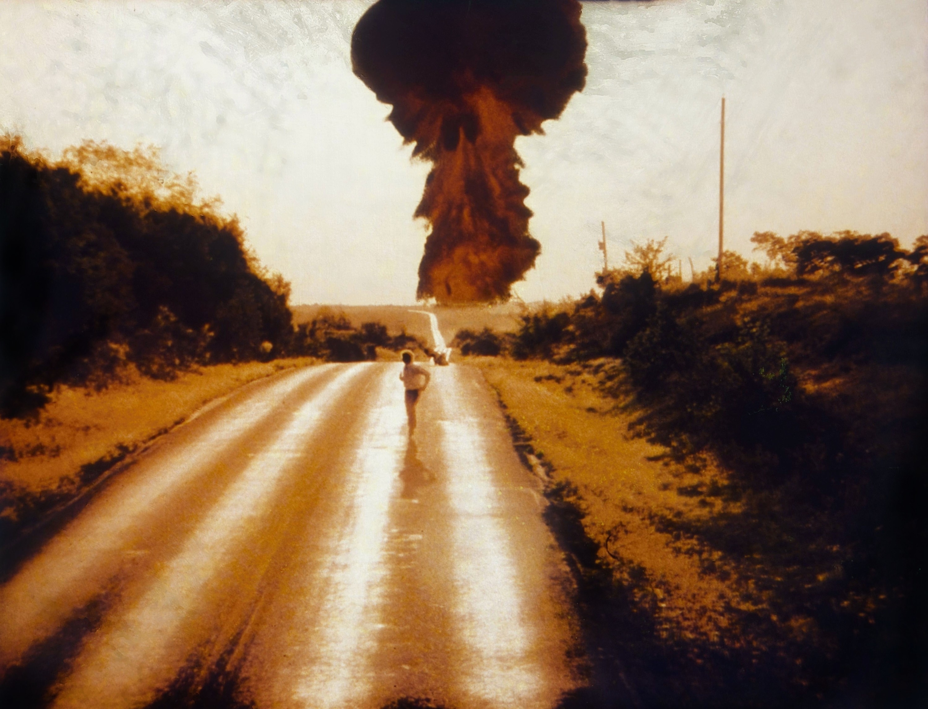 Historic photo of a large mushroom cloud in the distance viewed from a long road