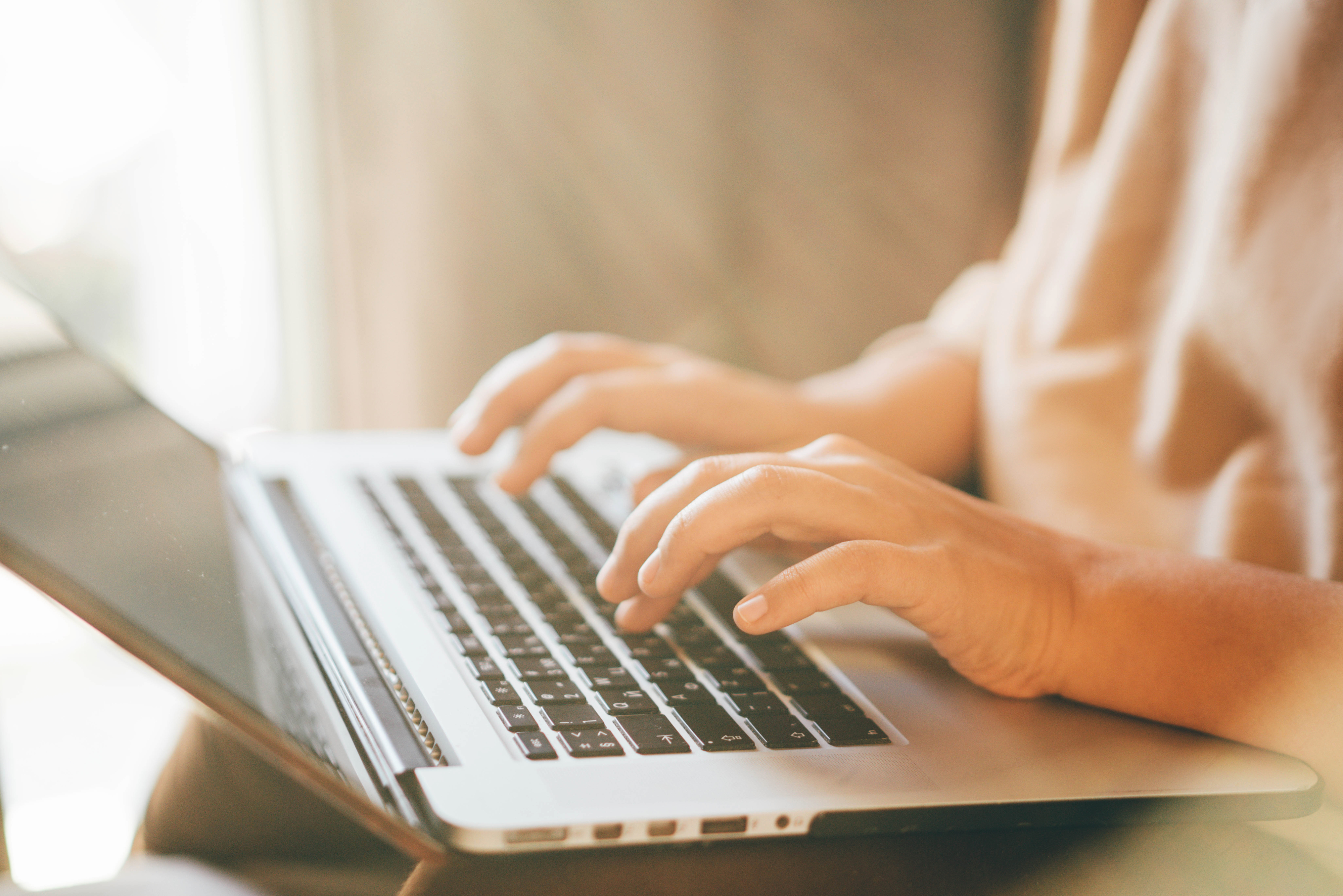 Close-up of a person's hands typing on a laptop keyboard