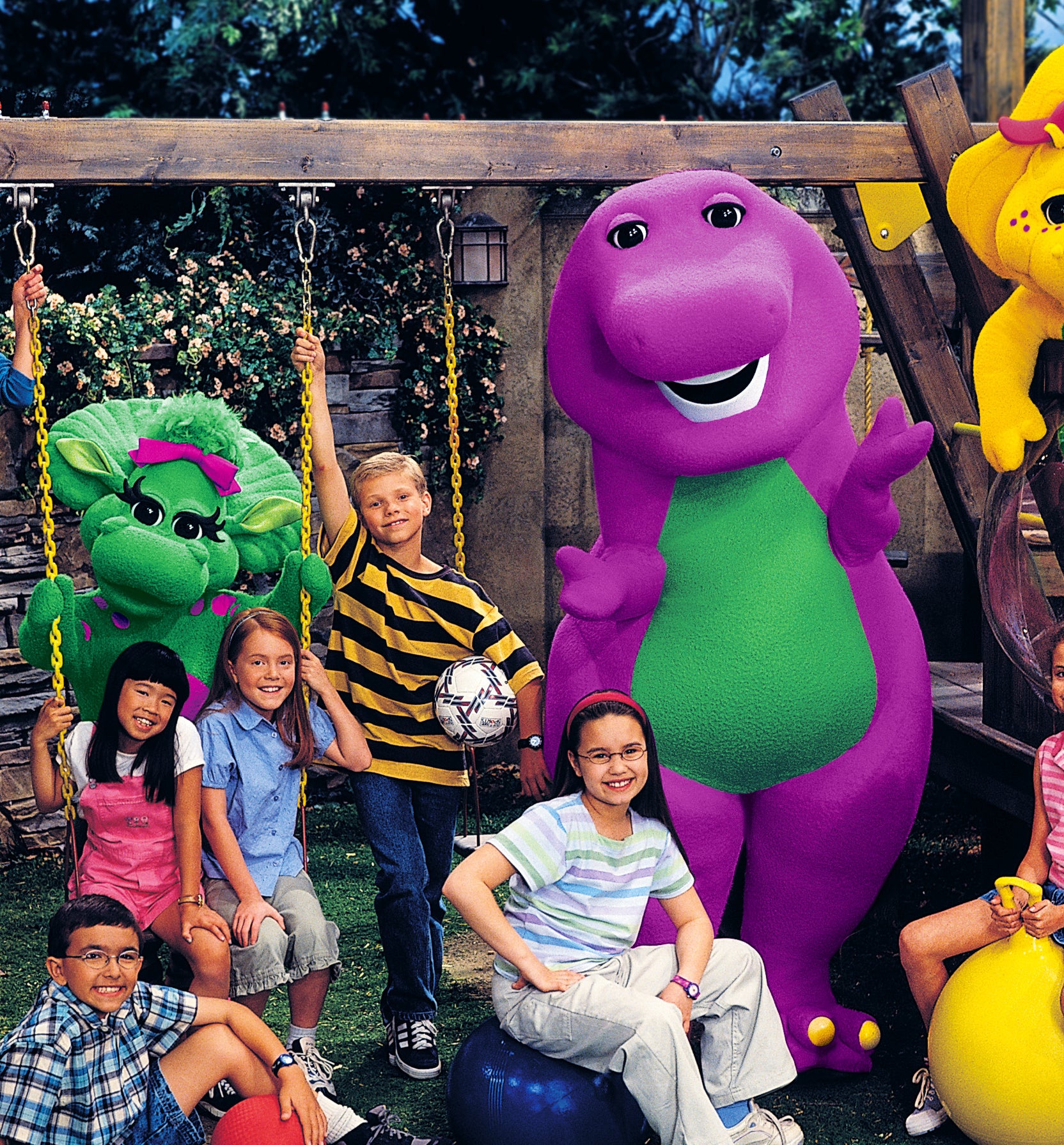Group of children posing with Barney the Dinosaur and friends BJ and Baby Bop on a playground
