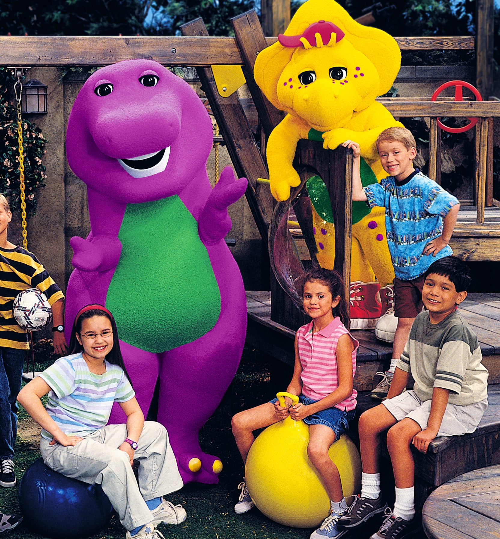 Group of children posing with Barney the Dinosaur and friends BJ and Baby Bop on a playground