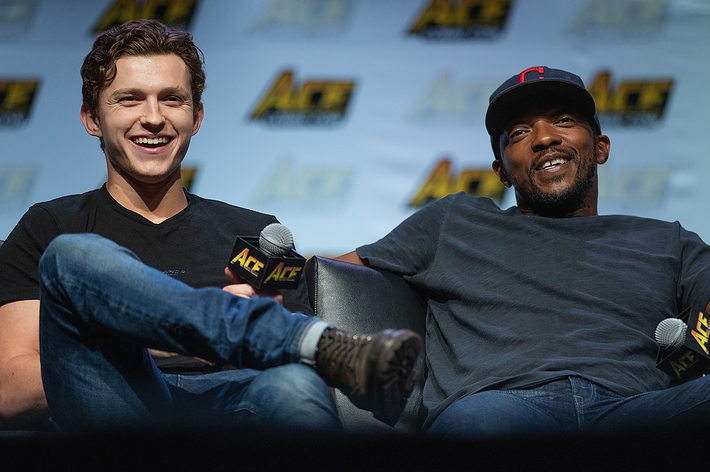 Tom Holland and Anthony Mackie sitting, laughing, holding microphones at a panel event