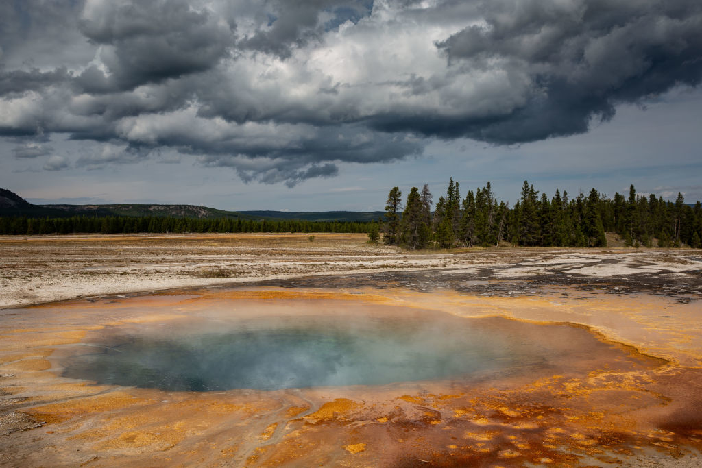 A geothermal hot spring with orange bacterial mats under a cloudy sky