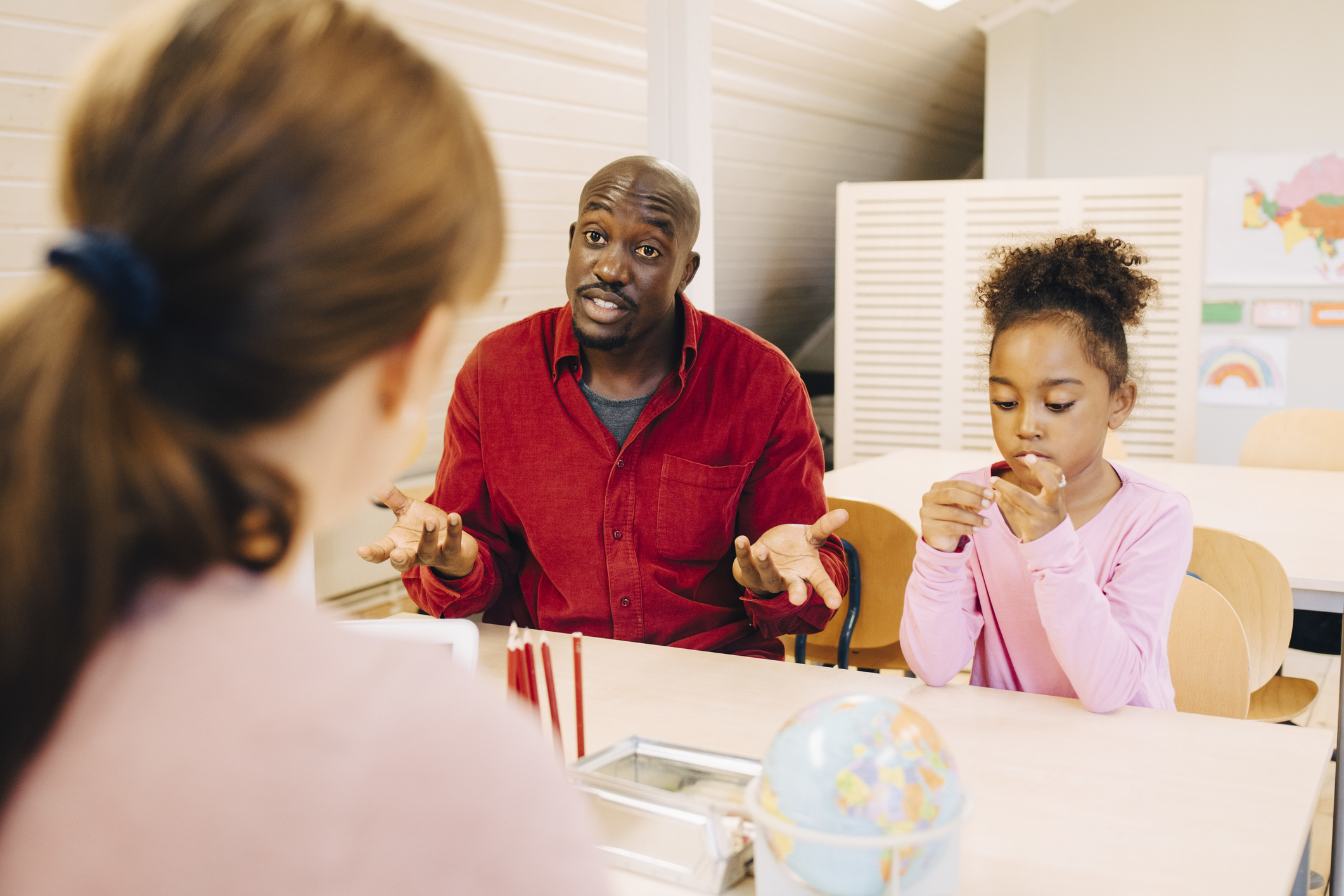 Adult explaining to child, child blowing bubbles at table, indoors, educational environment