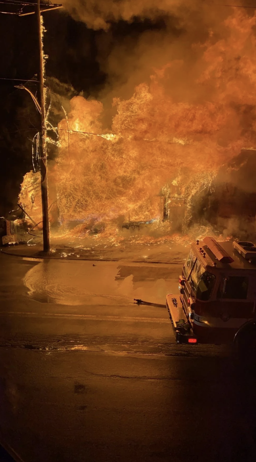 Firefighters battle a blaze at night, with a fire truck in the foreground