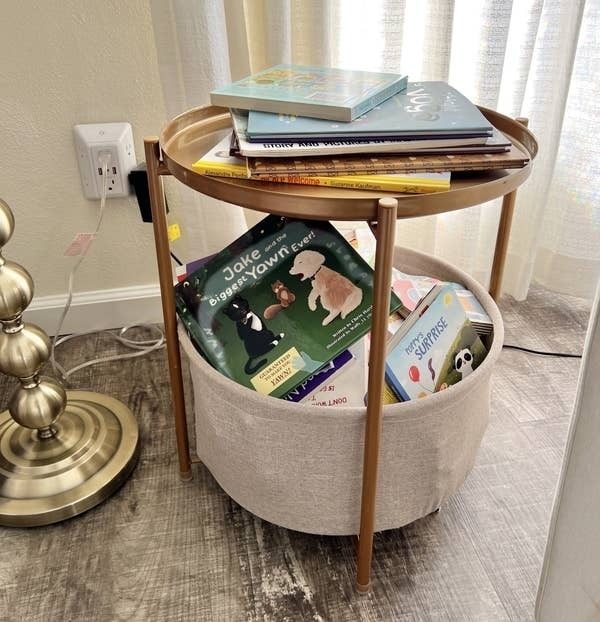 Round side table with books on top and in storage compartment, used for functional decor in a home
