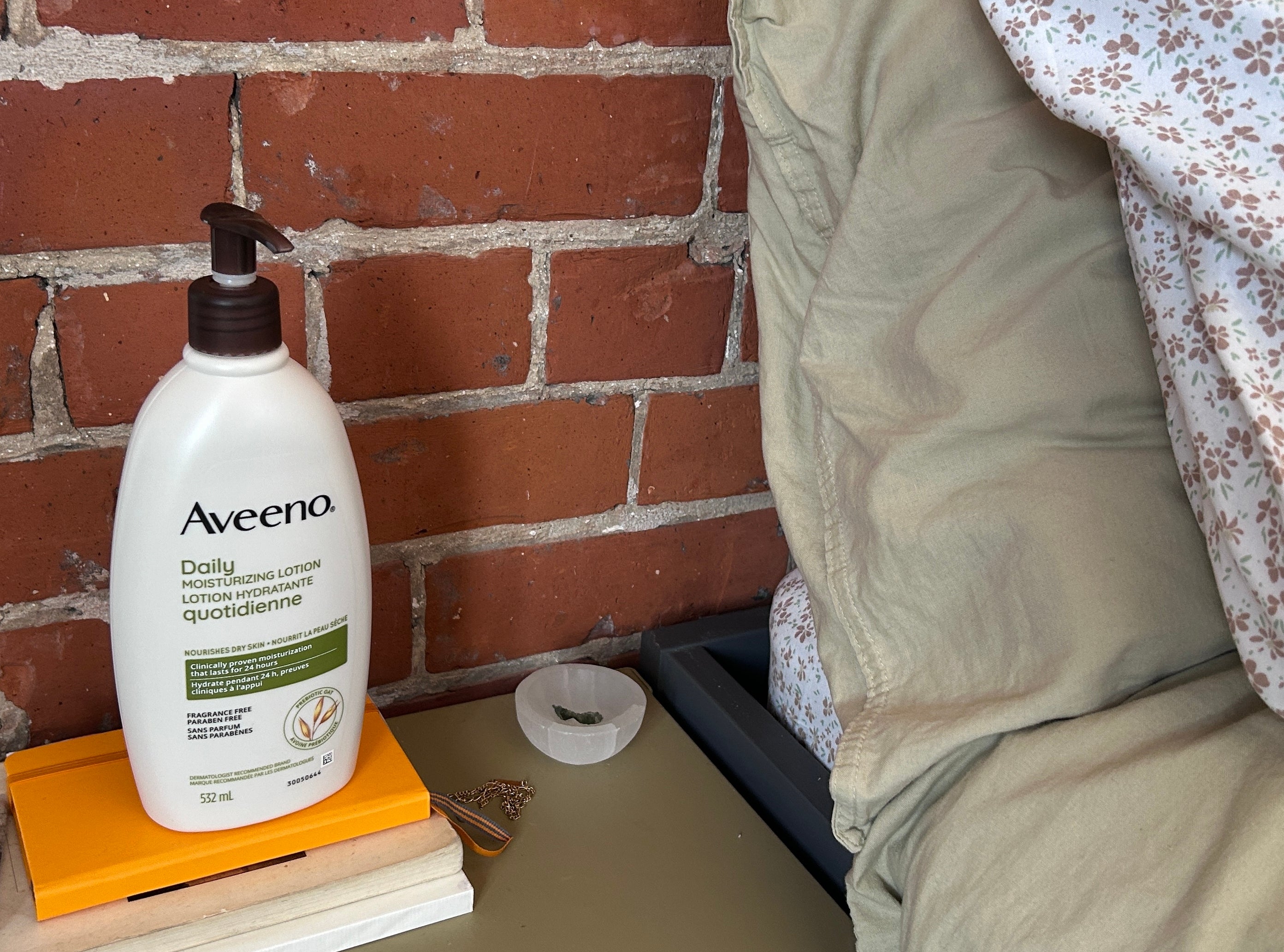 Aveeno lotion bottle on bedside table with books, decorative items, and bedding