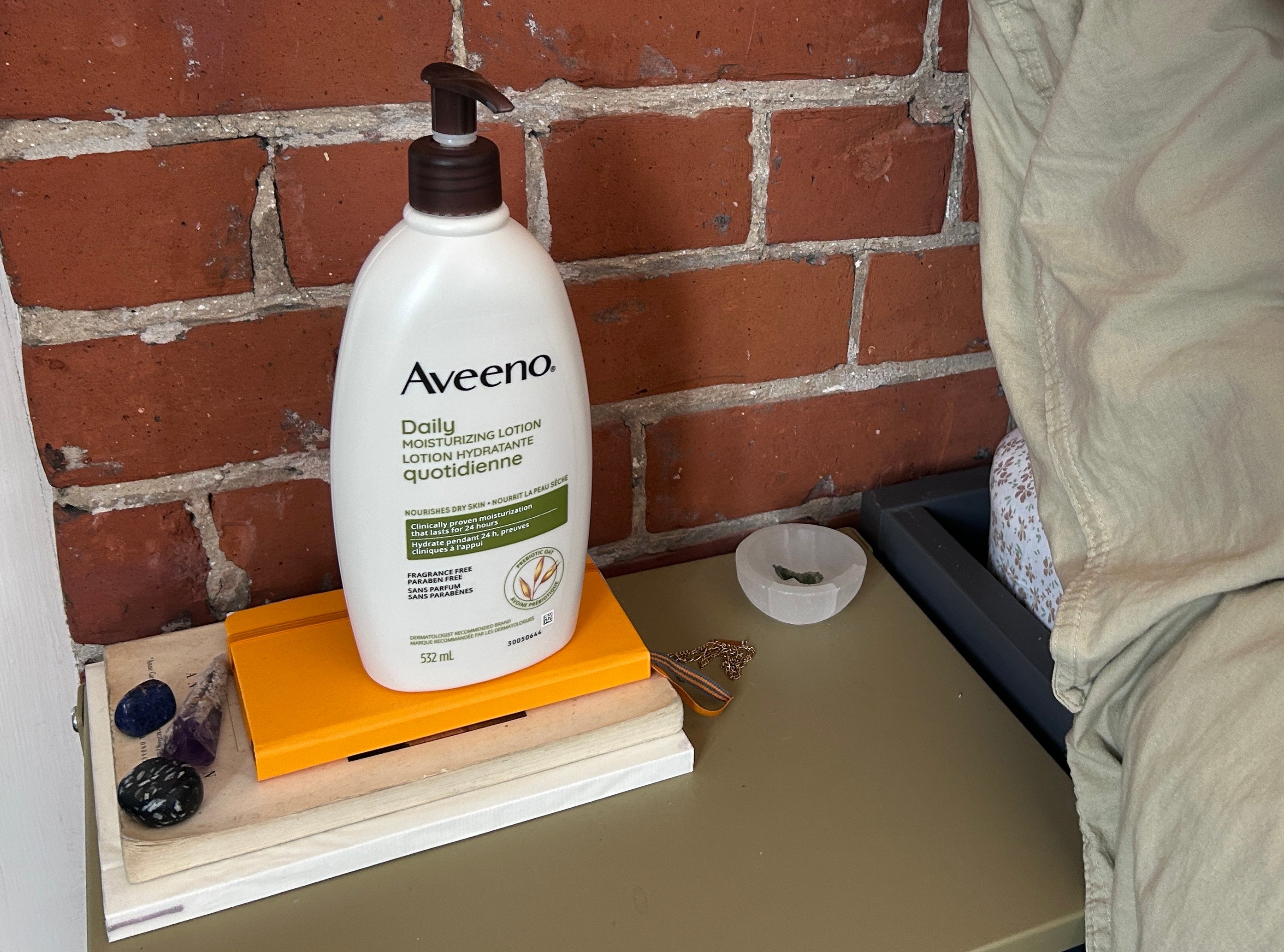 Aveeno lotion bottle on bedside table with books, decorative items, and bedding
