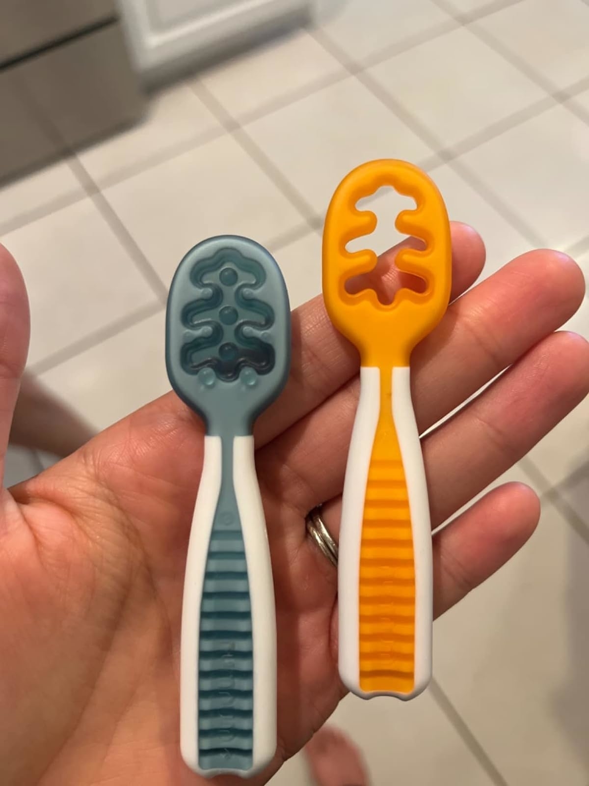 Two patterned silicone teething spoons held in a hand