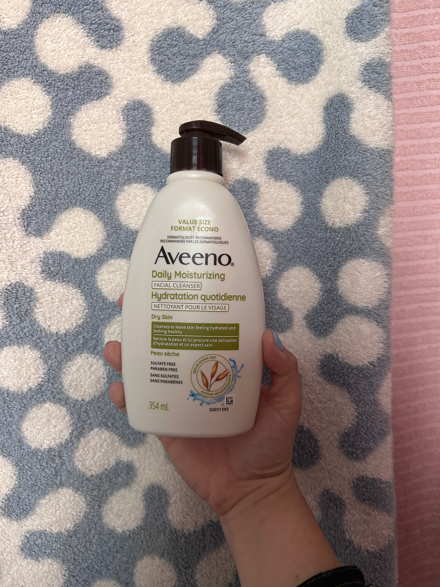 Person holding a bottle of Aveeno Daily Moisturizing Lotion against a patterned background