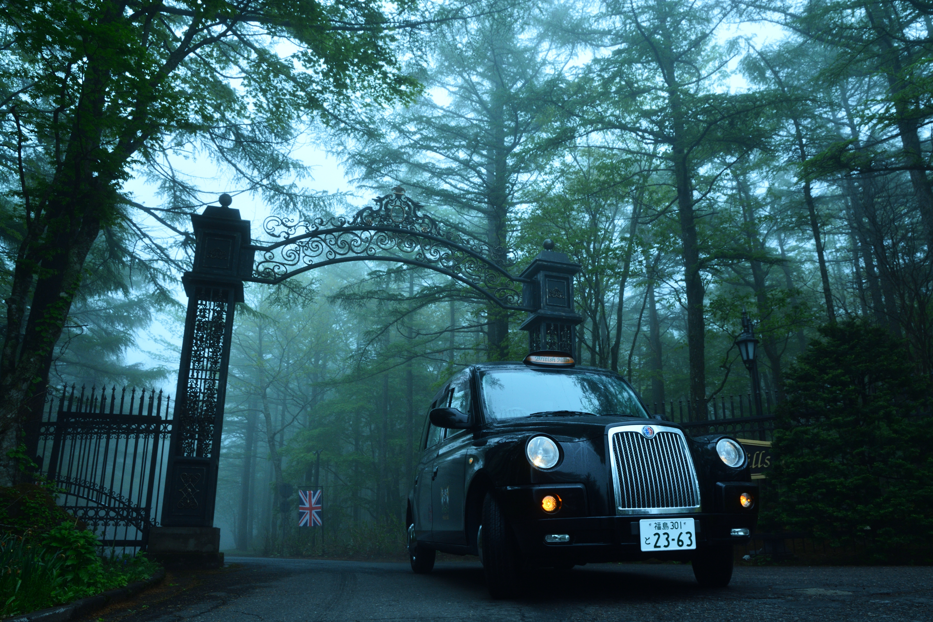 霧の中の森の中を走る黒のタクシー。