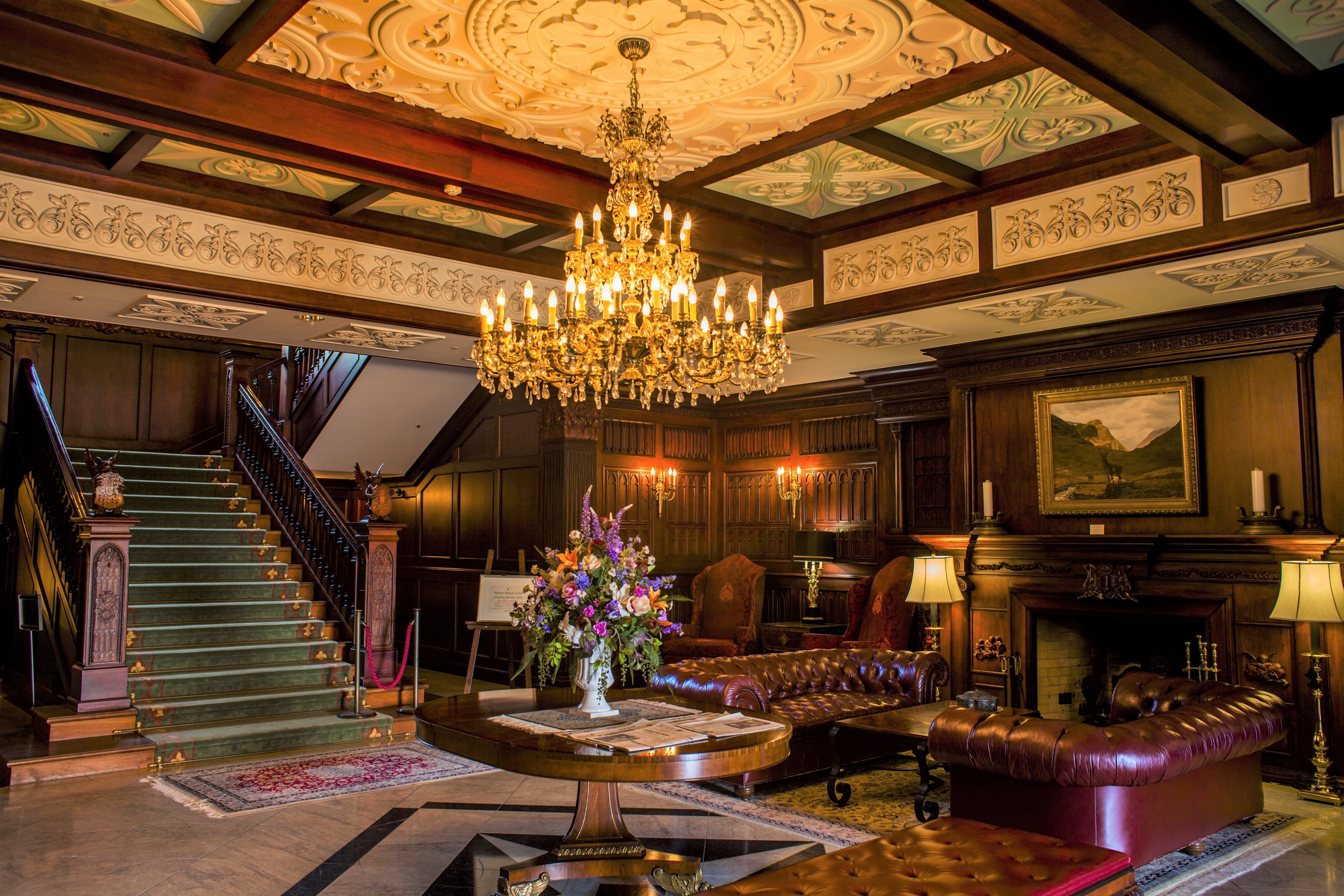豪華な内装の部屋、シャンデリア、暖炉、階段、中央に花束が飾られたテーブルがある。