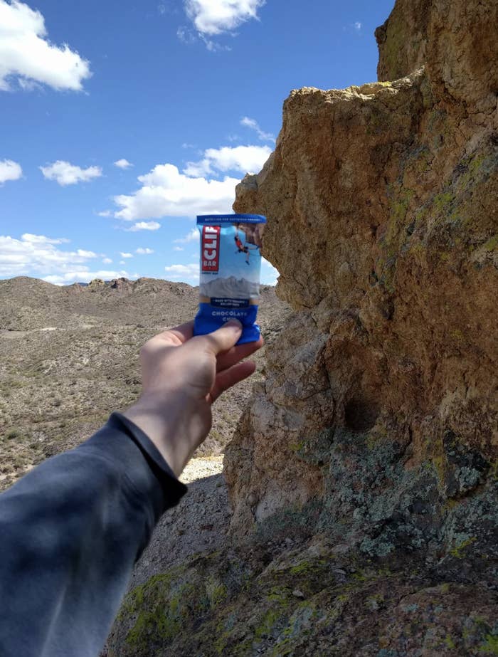 Person&#x27;s hand holding a Clif energy bar with rocky terrain in the background