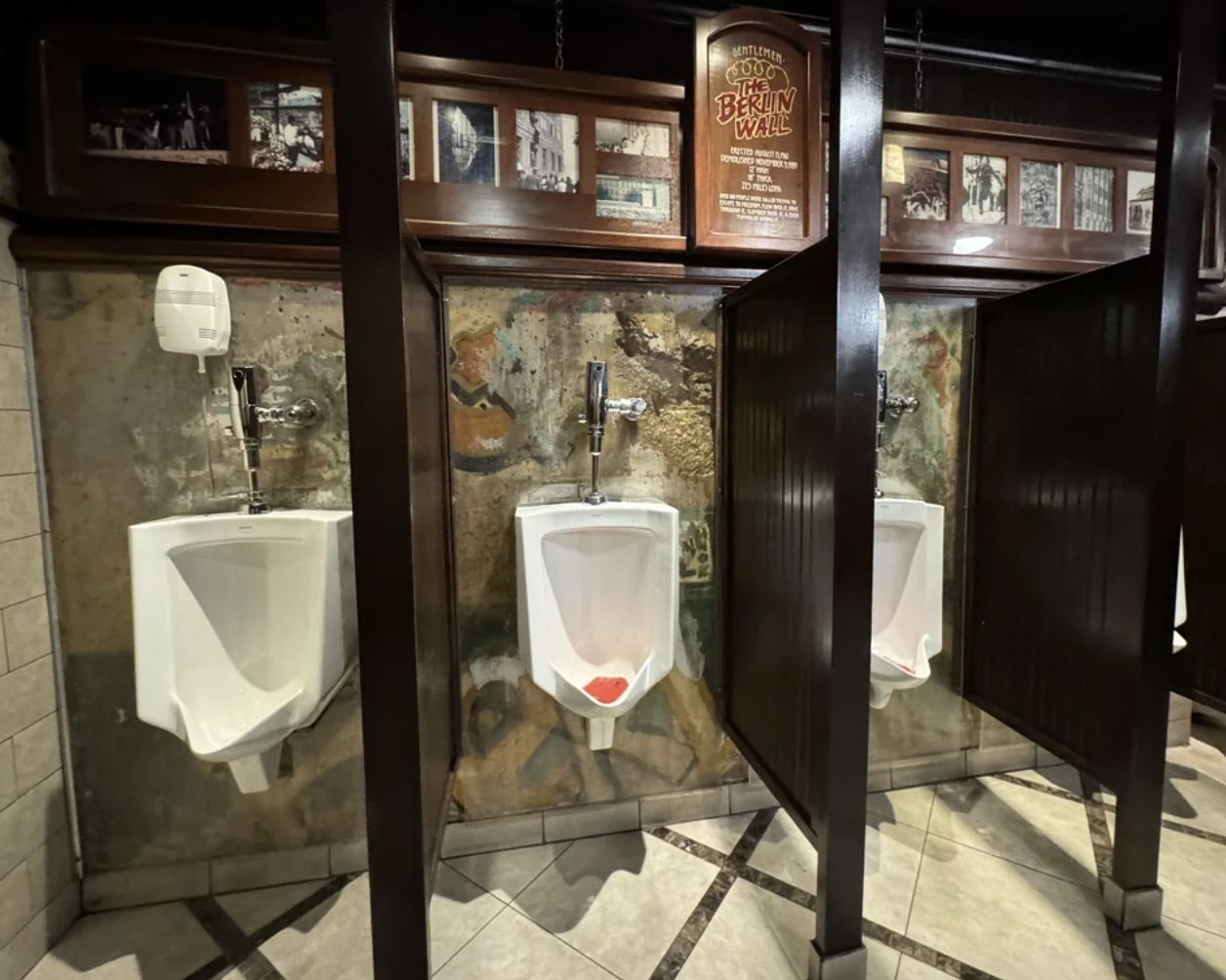 Public restroom with three urinals and hand sanitizer dispenser, featuring partitioned privacy